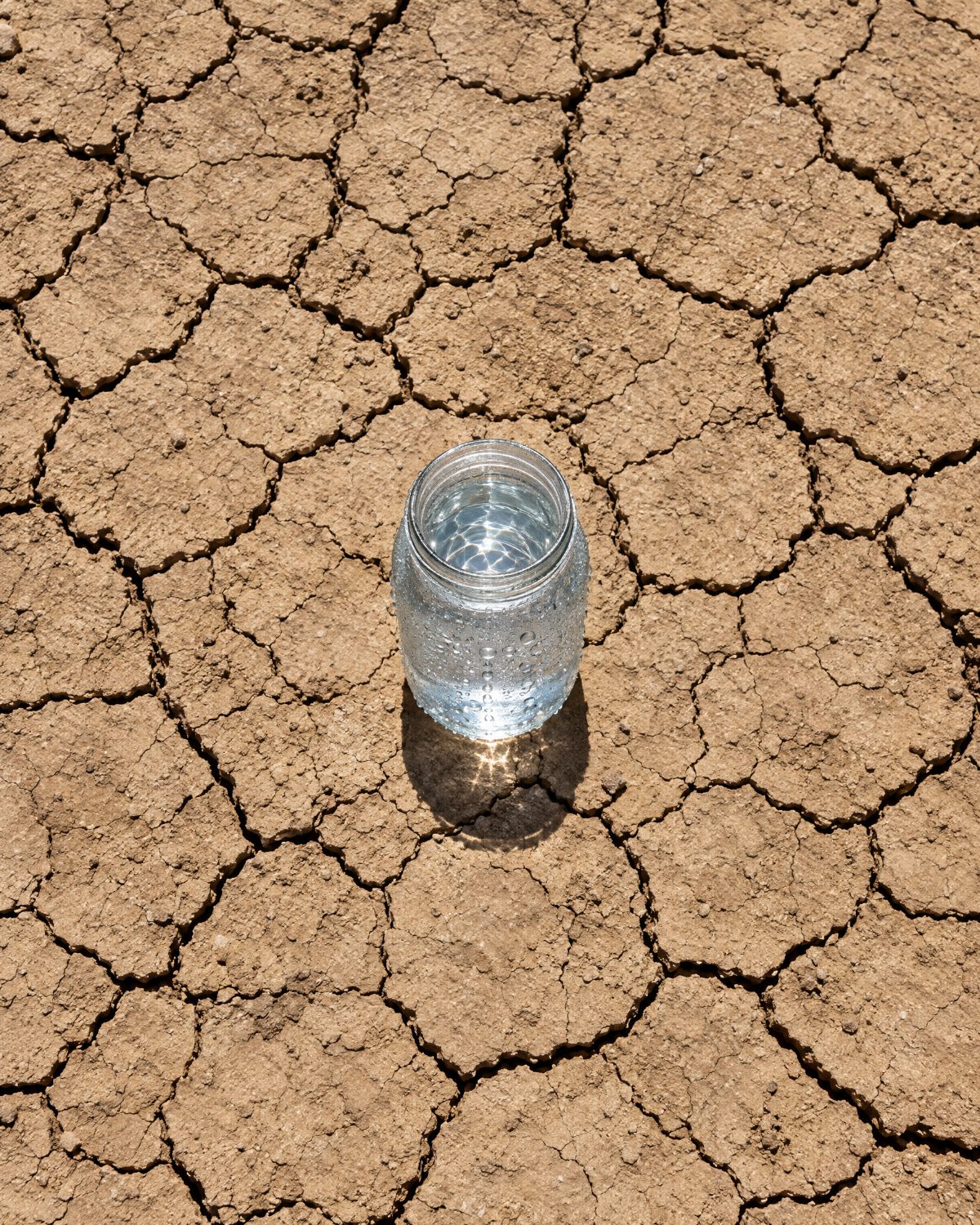 Glass jar of water on dry cracked ground